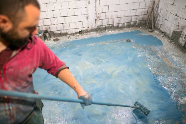 Man applying blue garage floor coating with a roller to concrete.