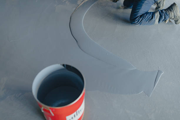 Worker applying fresh grey garage floor coating from a red bucket. Professional installation.
