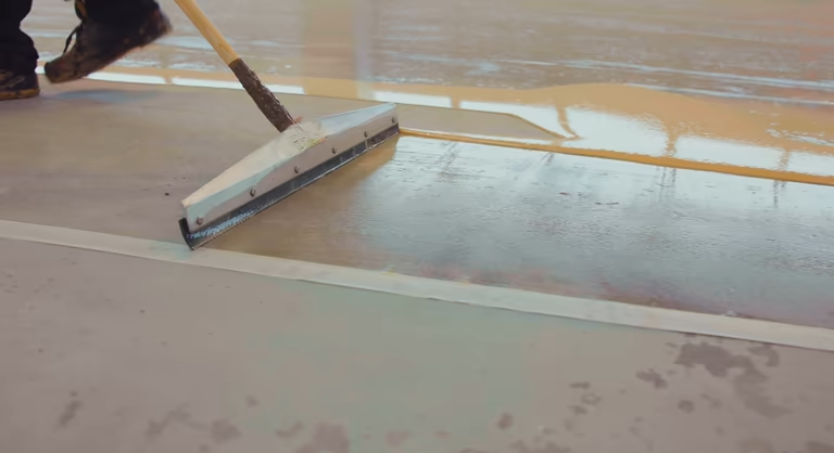 Applying new garage floor coating with a squeegee.