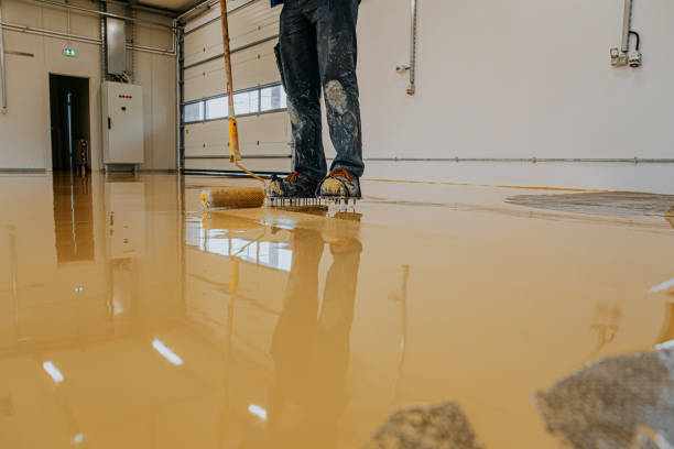 Worker applying a new yellow garage floor coating with a roller.
