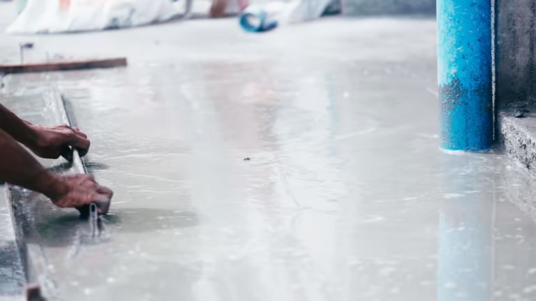 Hands smoothing a wet concrete surface, preparing for a garage floor coating.