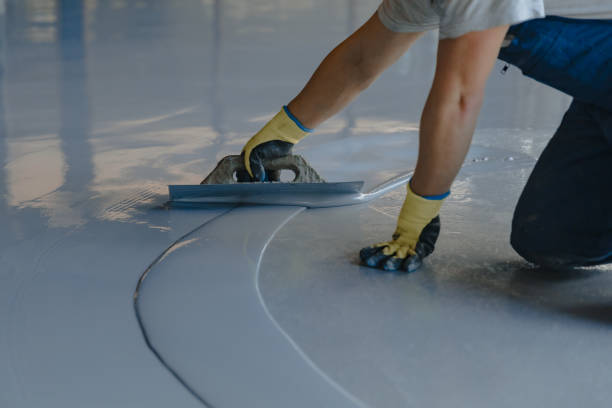 Worker applying a smooth, grey garage floor coating with a squeegee.