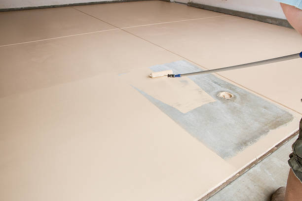 Applying light tan garage floor coating with a roller for a fresh look.