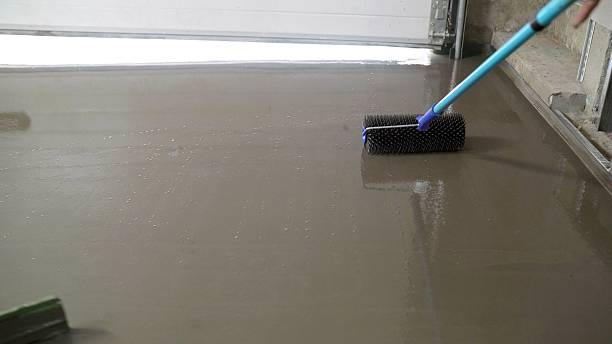 Spiked roller used to de-aerate new garage floor coating, ensuring a smooth finish.