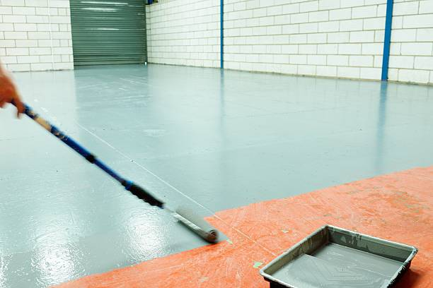 Applying light grey garage floor coating with a roller.