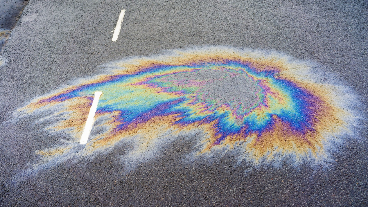 Oil slick on asphalt demonstrates damage prevented by garage floor coating.